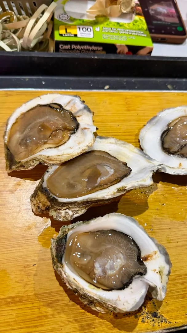 Four shucked Belcheri on a wooden board, the long heavy shells holding brown cream meat with a pale adductor scar